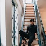 Modern portrait of a stylish woman seated on an indoor staircase in elegant attire.